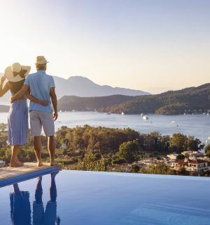 Loving couple on vacation time enjoys the summer sunset over the Aegean Sea by the swimming pool, Greece