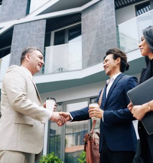 Happy business partners shaking hands when meeting outside the office building view from below