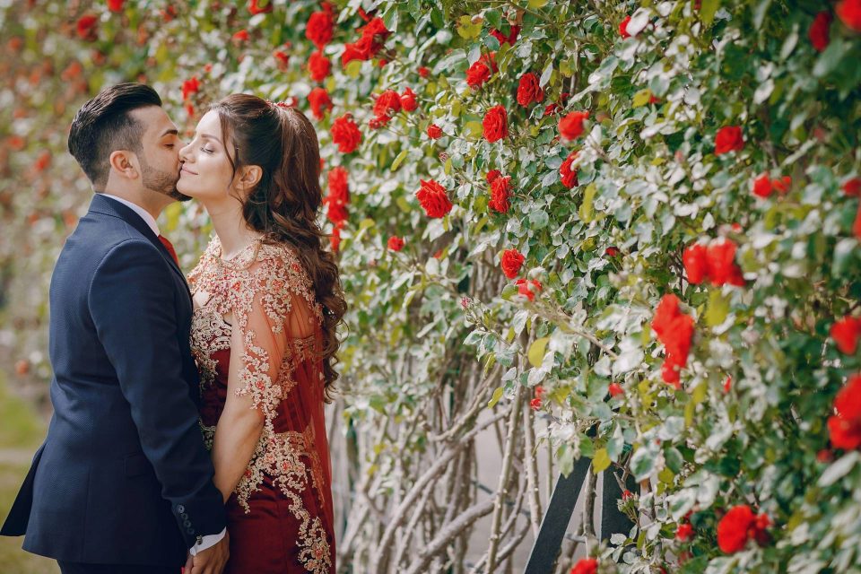 Beautiful woman in a long red dress walks around the city with her husband in a blue suit and with a beard