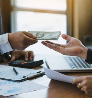 businessman giving money to his partner on office desk , bribery and corruption concepts.